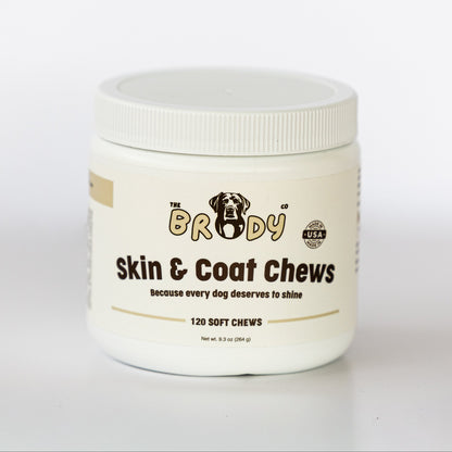 A white plastic jar of 'The Brody Co' Skin & Coat Chews for dogs, featuring a white screw-top lid and a cream-colored label with black and gold text.