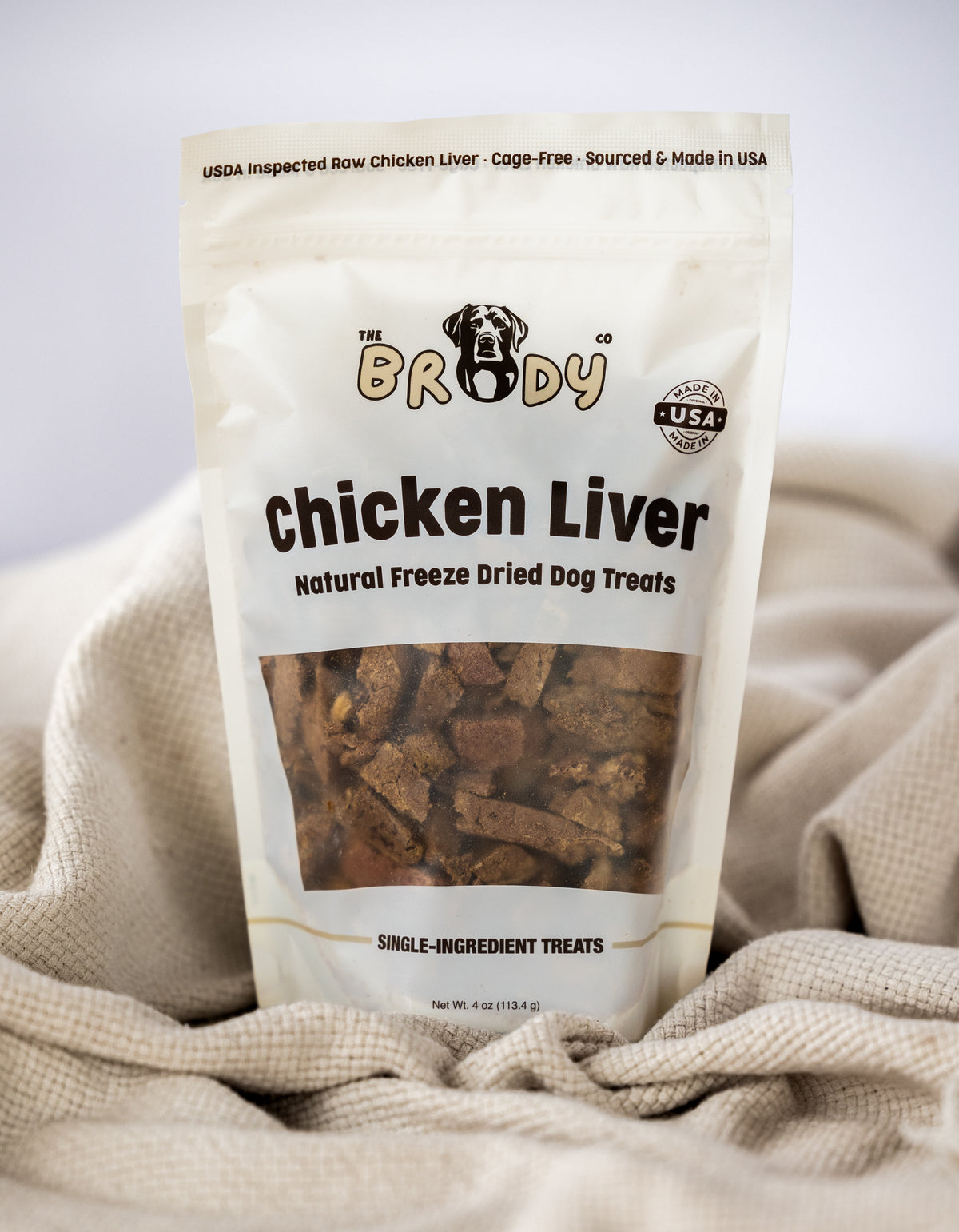 A stand-up pouch of The Brady Co. Chicken Liver freeze dried dog treats, resting on a textured beige linen fabric background.