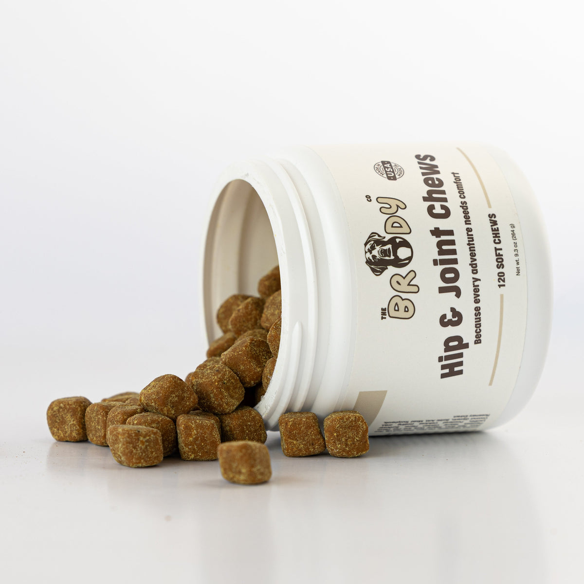 A white plastic jar of ERGO+ Hip & Joint Chews for dogs, tipped over with the brown chewable treats spilling out onto a clean white surface.