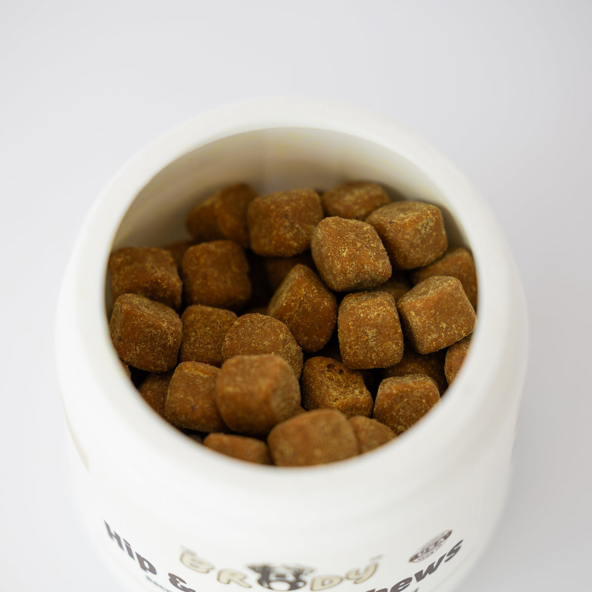 Brown chew supplements pieces visible inside an open white bowl, photographed from above on a clean white background.