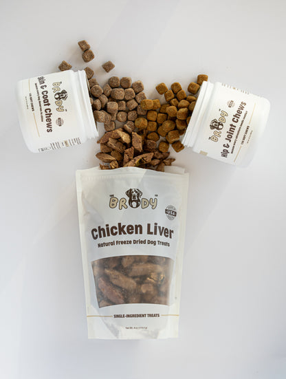 Three white containers of The Brody Co pet supplements and a large resealable pouch of Chicken Liver natural joint support treats, with some brown kibble chews spilled on a clean white background.
